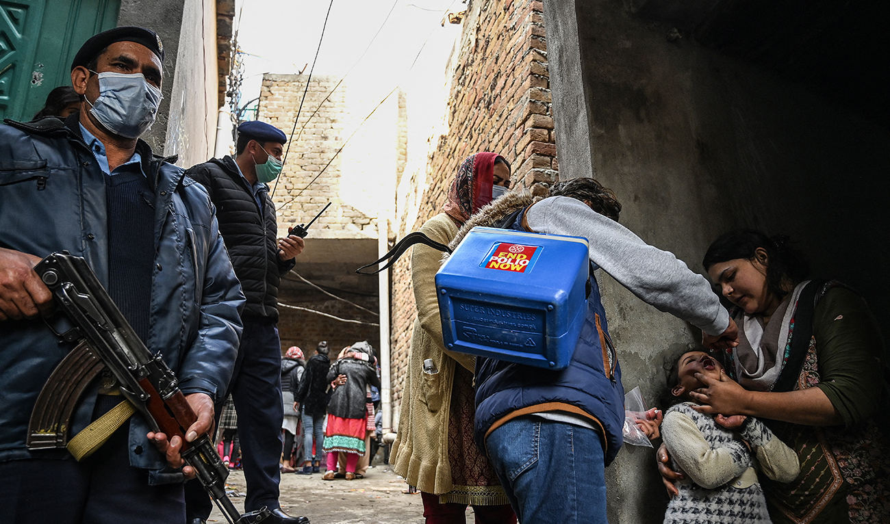 Policemen stand guard as a health worker (C) administers polio vaccine drops to a child during a polio vaccination door-to-door campaign in a slum area in Islamabad on January 13, 2021. (AFP/File)