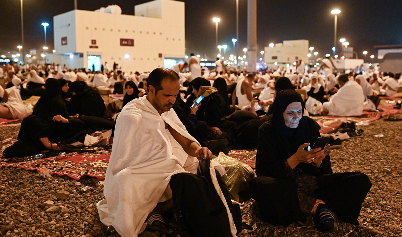 Muslim pilgrims browse their phones as they rest after arriving at Muzdalifah before heading to Mina during the annual Muslim Hajj pilgrimage on June 27, 2023. (AFP/File)