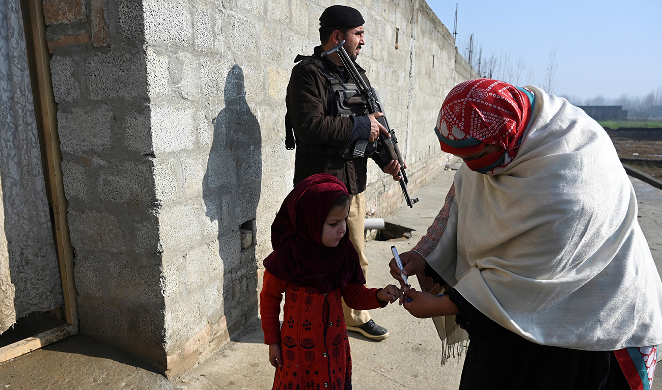 In this picture taken on January 24, 2022, a health worker marks the finger of a child after administering a polio vaccine as a policeman (top) stands guard during a door-to-door polio vaccination campaign on the outskirts of Mardan, in the Pakistan's Khyber Pakhtunkhwa province. (AFP/File)
