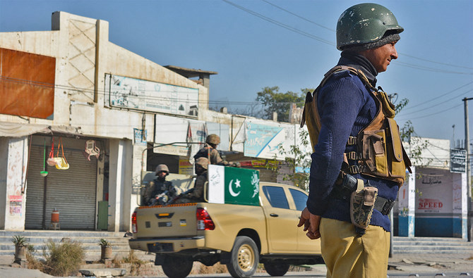 A policeman (R) and army soldiers (L) stand guard along a road in Bannu on December 21, 2022. (AFP/File)