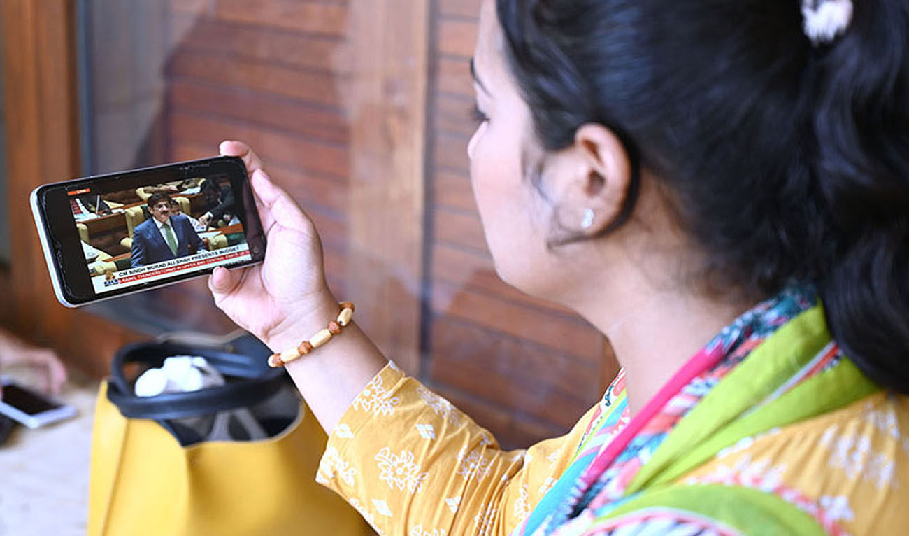 A woman listens the Sindh Chief Minister Syed Murad Ali Shah’s budget speech on her mobilephone in Karachi on June 14, 2024. (APP)