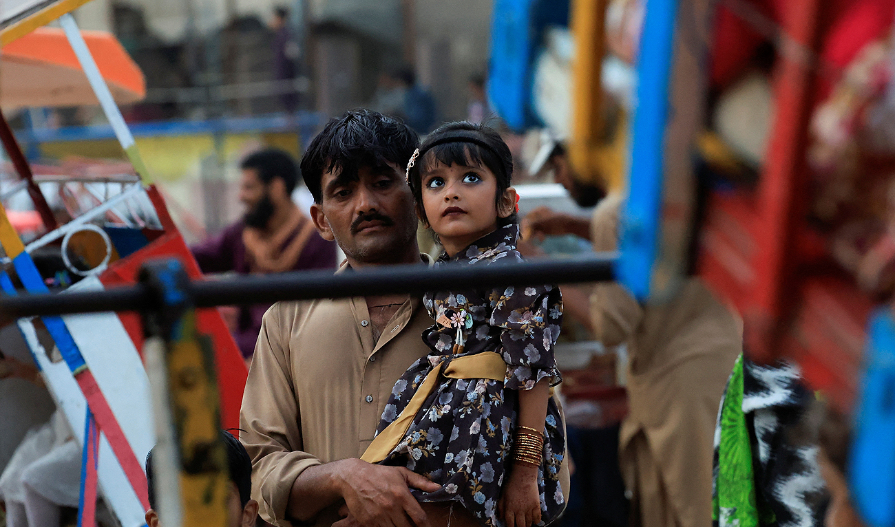 A father holds up his daughter while waiting for her turn to ride on a swing, on the second day of Eid Al-Adha celebrations, in Karachi, Pakistan June 18, 2024. (REUTERS)