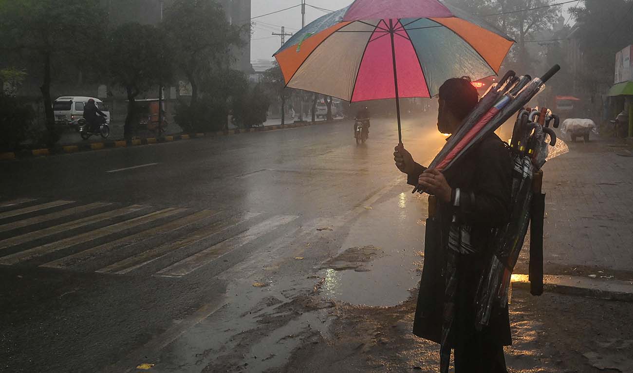 A street vendor carries umbrellas as he waits for customers along a road during a rain shower in Lahore on January 19, 2022. (AFP/File)