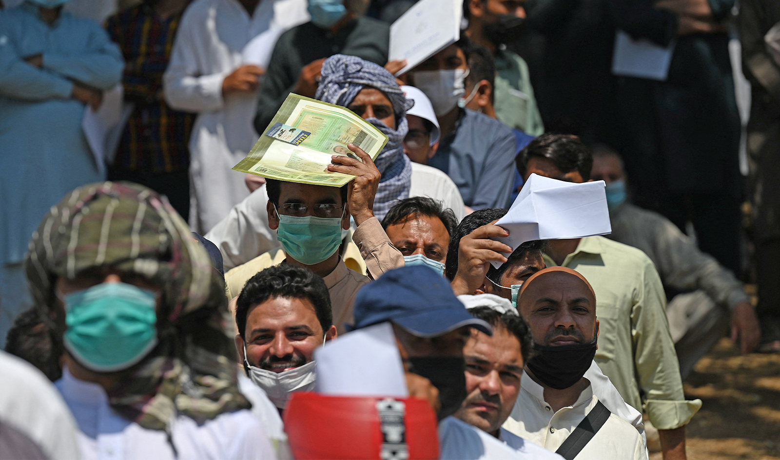 In this picture taken on May 19, 2021, Pakistani nationals, wearing face masks amid concerns over the spread of the Covid-19 coronavirus, wait in a queue to apply for a visa outside Afghanistan's embassy in Islamabad. (AFP/File)