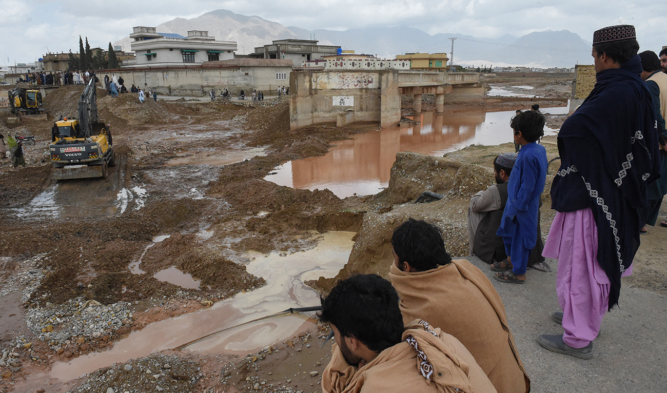 Onlookers gaze towards municipal workers using heavy machinery to level the ground after damage due to floodwaters following heavy rains on the outskirts of Quetta on April 15, 2024. (AFP/File)