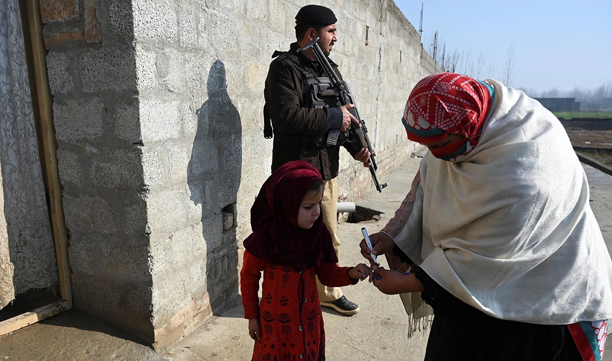 In this picture taken on January 24, 2022, a health worker marks the finger of a child after administering a polio vaccine as a policeman (top) stands guard during a door-to-door polio vaccination campaign on the outskirts of Mardan, in the Pakistan's Khyber Pakhtunkhwa province. (AFP/File)