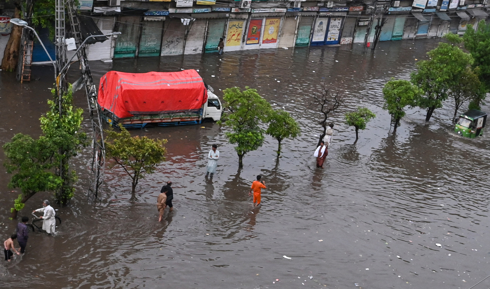 Commuters make their way through a flooded street after a heavy rainfall near row of shops in Lahore on July 1, 2024. (AFP/File)
