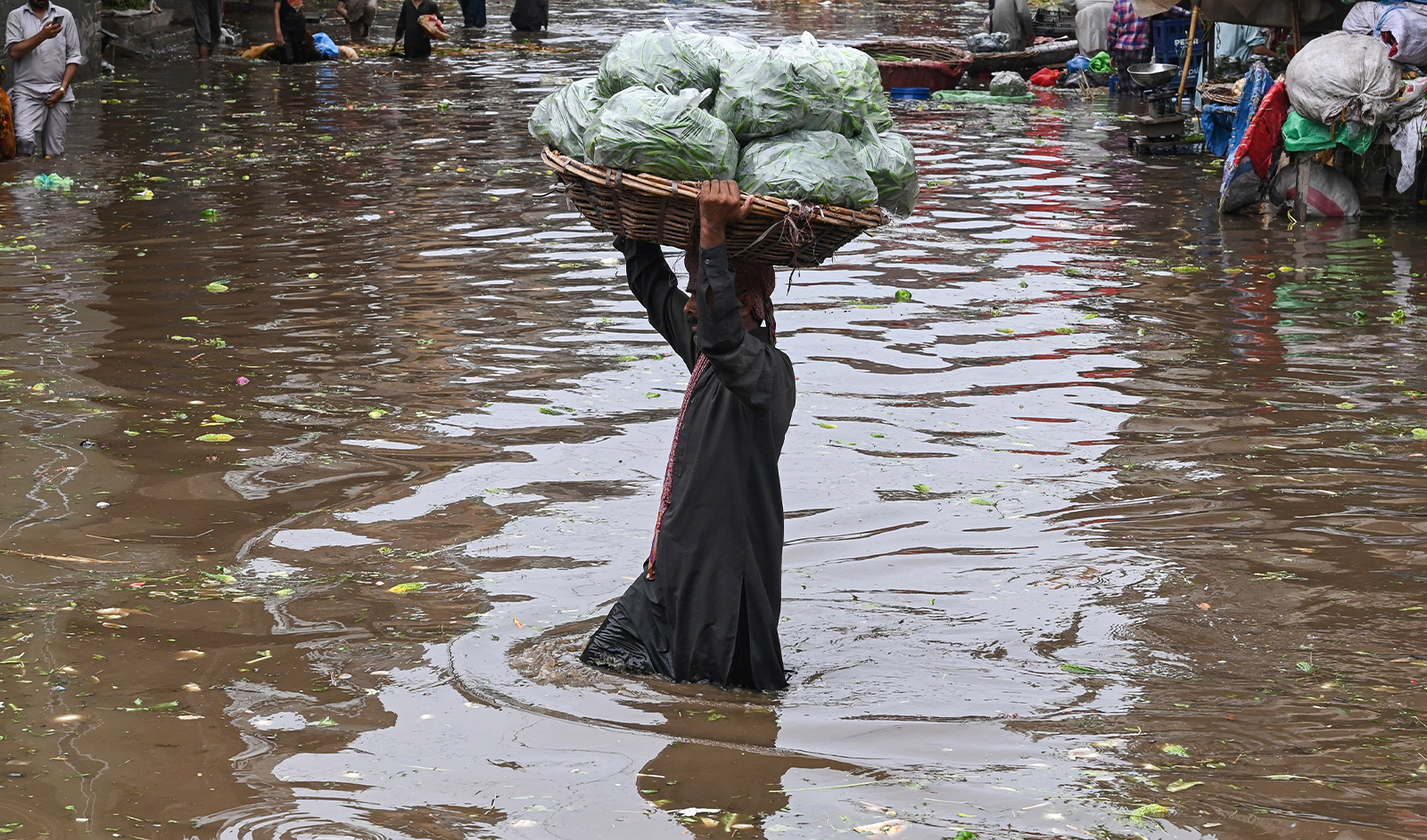 Workers carry vegetables as they wade through a flooded street at a market after a heavy rainfall in Lahore on July 1, 2024. (AFP/File)