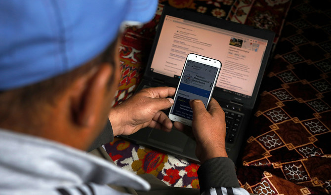 In this file photo, taken on October 9, 2023, a man monitors a metrological website on his mobile phone and laptop, at home in Hassanabad village, Pakistan. (REUTERS/File)
