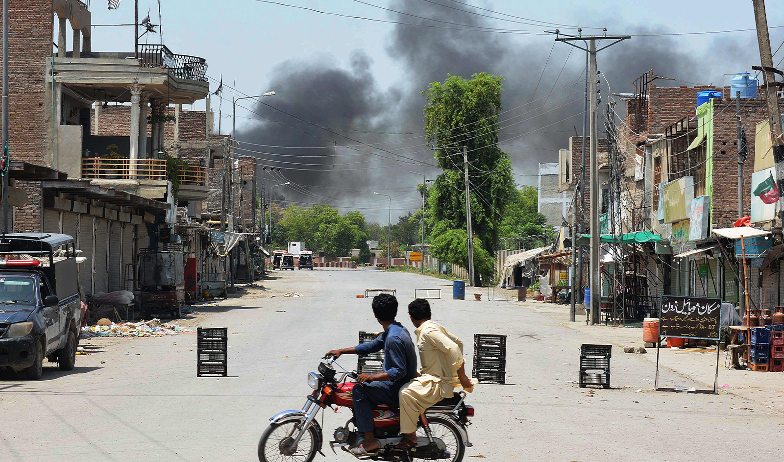 Men riding a bike watch as smoke rises following an explosion allegedly after militants suicide squad attempted to storm an army cantonment that houses military residences and offices in Bannu on July 15, 2024. (AFP)