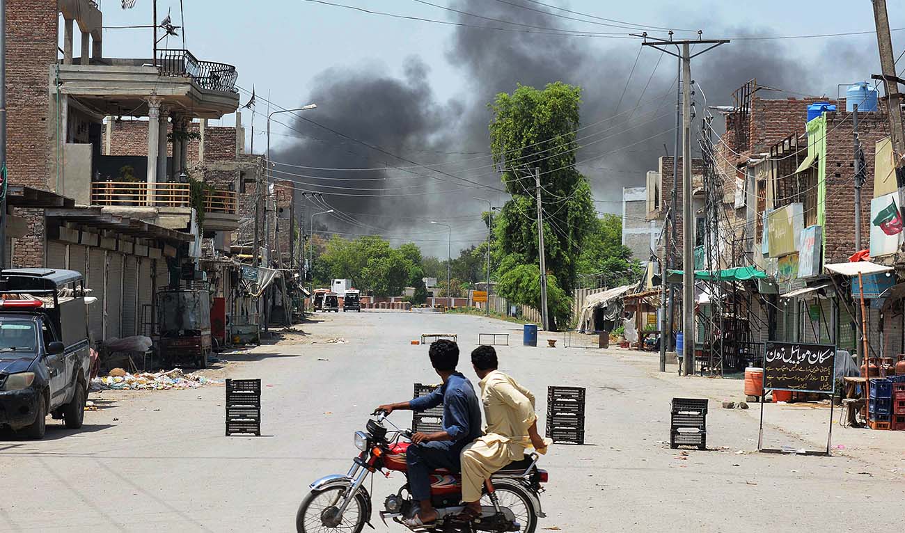 Men riding a bike watch as smoke rises following an explosion allegedly after militants suicide squad attempted to storm an army cantonment that houses military residences and offices in Bannu on July 15, 2024. (AFP)