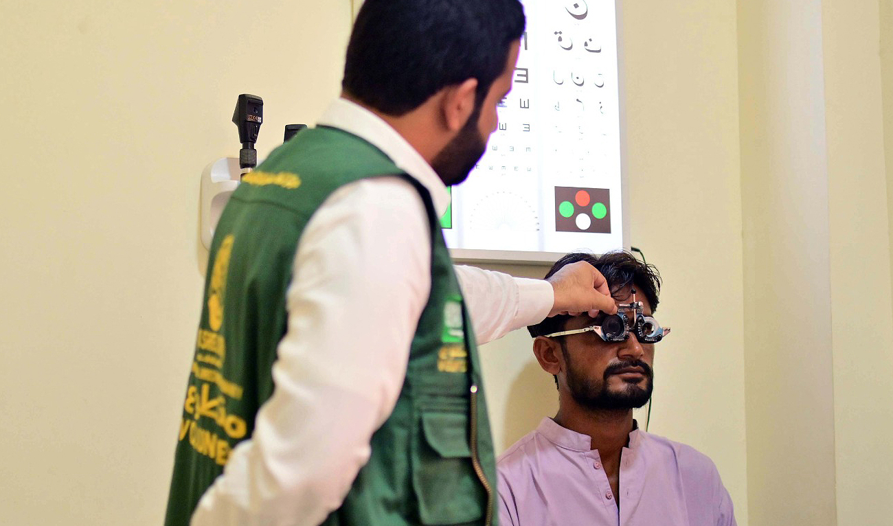 In this handout photograph, taken and released by Saudi Arabia’s King Salman Humanitarian Aid and Relief Center on July 25, 2024, Pakistani volunteer adjusts an interpupillary distance test frame as he checks the eyes of a patient at Al-Ibrahim Eye Hospital in Karachi. (Photo courtesy: KSrelief)
