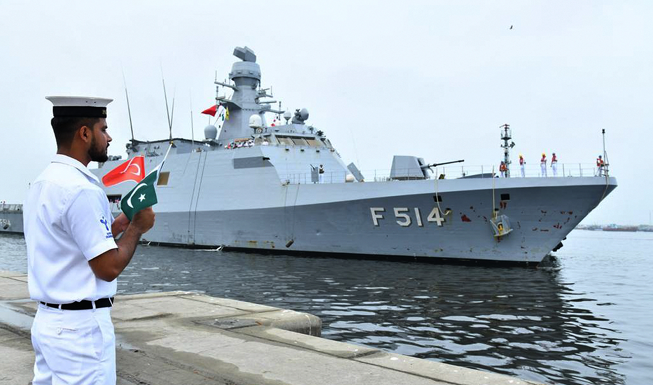 In this handout photograph, taken and released by Director General Public Relations Pakistan Navy on July 30, 2024, Pakistan Navy official holds national flags of Pakistan and Turkiye as Turkish Navy Ship TCG KINALIADA (F-514) arrived in Karachi. (Photo courtesy: Pakistan Navy)