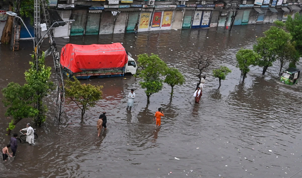 Commuters make their way through a flooded street after a heavy rainfall near row of shops in Lahore on July 1, 2024. (AFP/File)