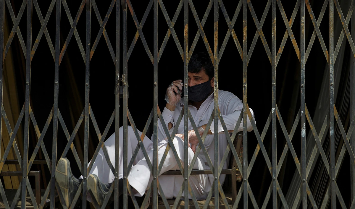 A man wearing a facemask speaks on his mobile phone sitting behind a closed gate during a government-imposed lockdown as a preventive measure against the COVID-19 novel coronavirus in Rawalpindi on March 25, 2020. (AFP/File)