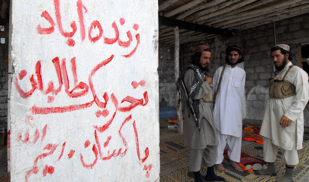 Armed militants of Tehreek-e-Taliban Pakistan (TTP), stand next to a graffiti which read as "Long Live Tehreek-e-Talban Pakistan" at a camp in a Pakistani tribal district of Mohmand Agency on July 21, 2008. (AFP/File)