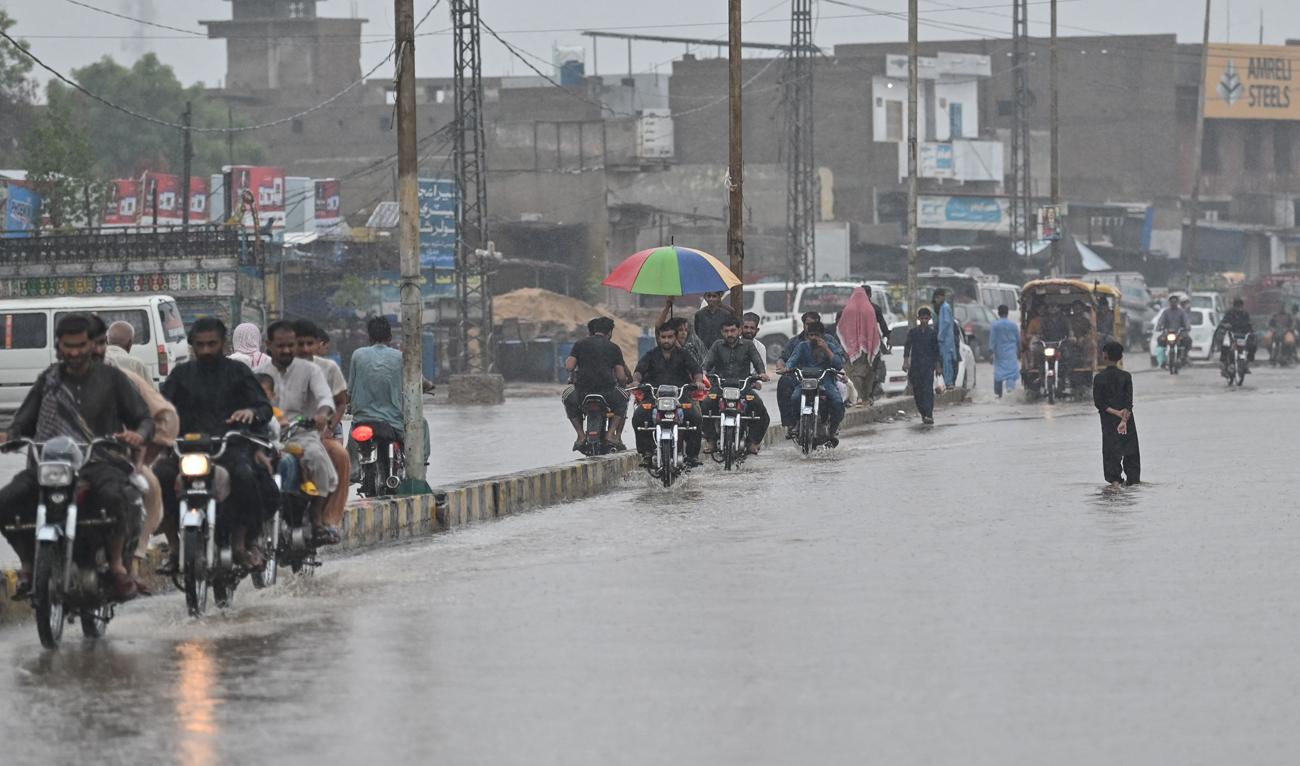 Commuters make their way along a street during rainfall in Dadu on August 4, 2024. (AFP)