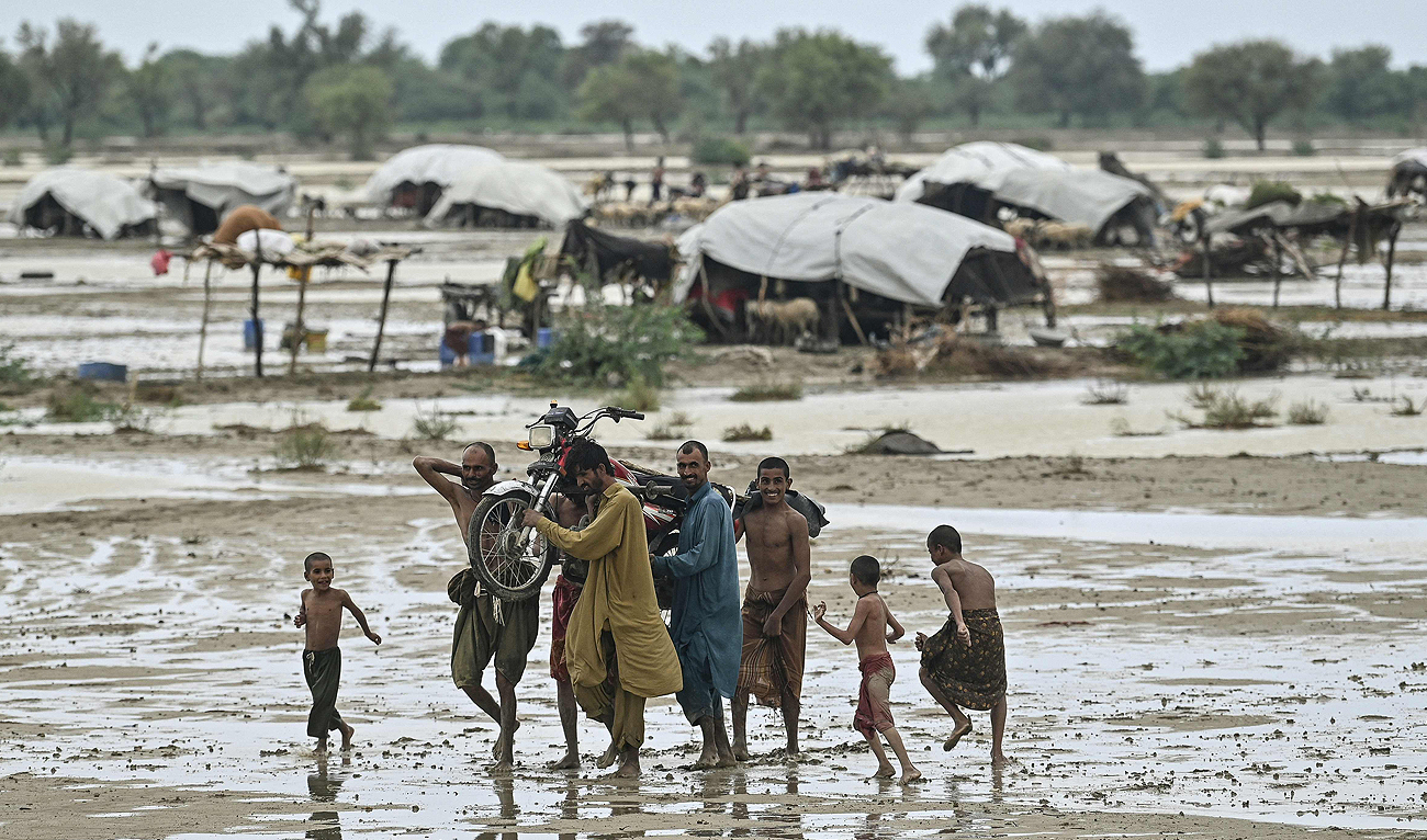 In this photograph taken on August 4, 2024, people carrying a motorcycle, walk across an agricultural land following rain in the aftermath of monsoon floods at Johi, Dadu district in Sindh province. (AFP/File)