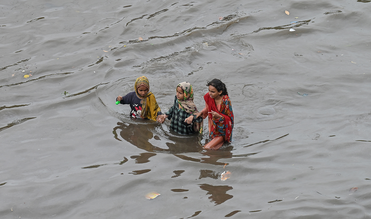 Girls wade through a flooded street amid heavy rainfall in Lahore on August 1, 2024. (AFP/File)