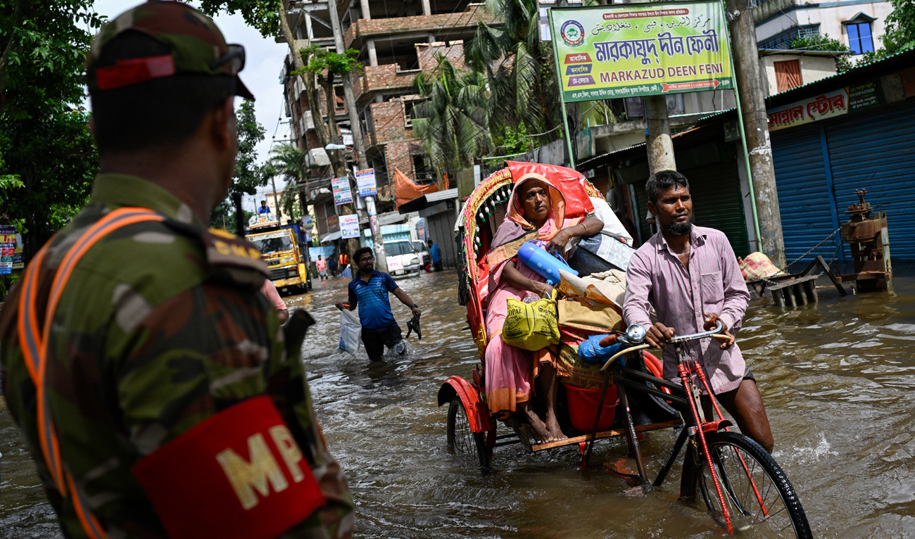 A Bangladeshi army soldier watches as people carrying their belongings wade through flooded water to reach a relief center in Feni, a coastal district in southeast Bangladesh on August 23, 2024. (AP)