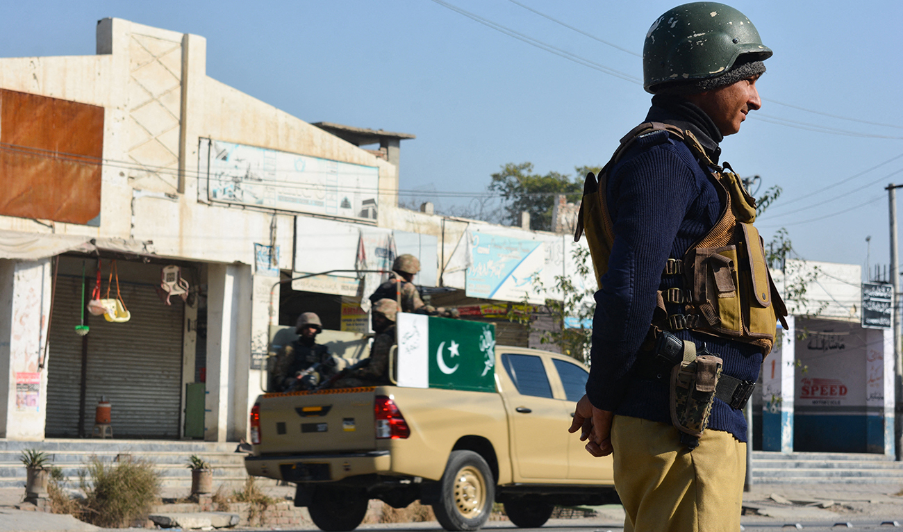 A policeman (R) and army soldiers (L) stand guard along a road in Bannu on December 21, 2022. (AFP/File)
