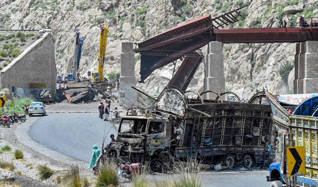 Residents stand beside a charred vehicle near a collapsed railway bridge the morning after a blast by separatist militants at Kolpur in Bolan district, Balochistan province on August 27, 2024. (AFP)