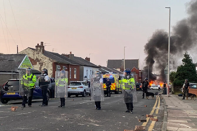 In this photo taken on July 30, 2024, smoke billows from a fire started by protesters as riot police stand guard after disturbances near the Southport Islamic Society Mosque in Southport, northwest England, a day after a deadly child knife attack. (AFP/File)