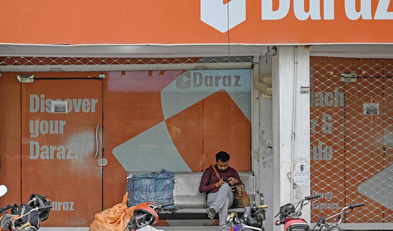 A man uses his mobile phone while sitting outside the office of Daraz, an e-commerce platform based out of Pakistan, in Islamabad on August 16, 2024. (AFP)