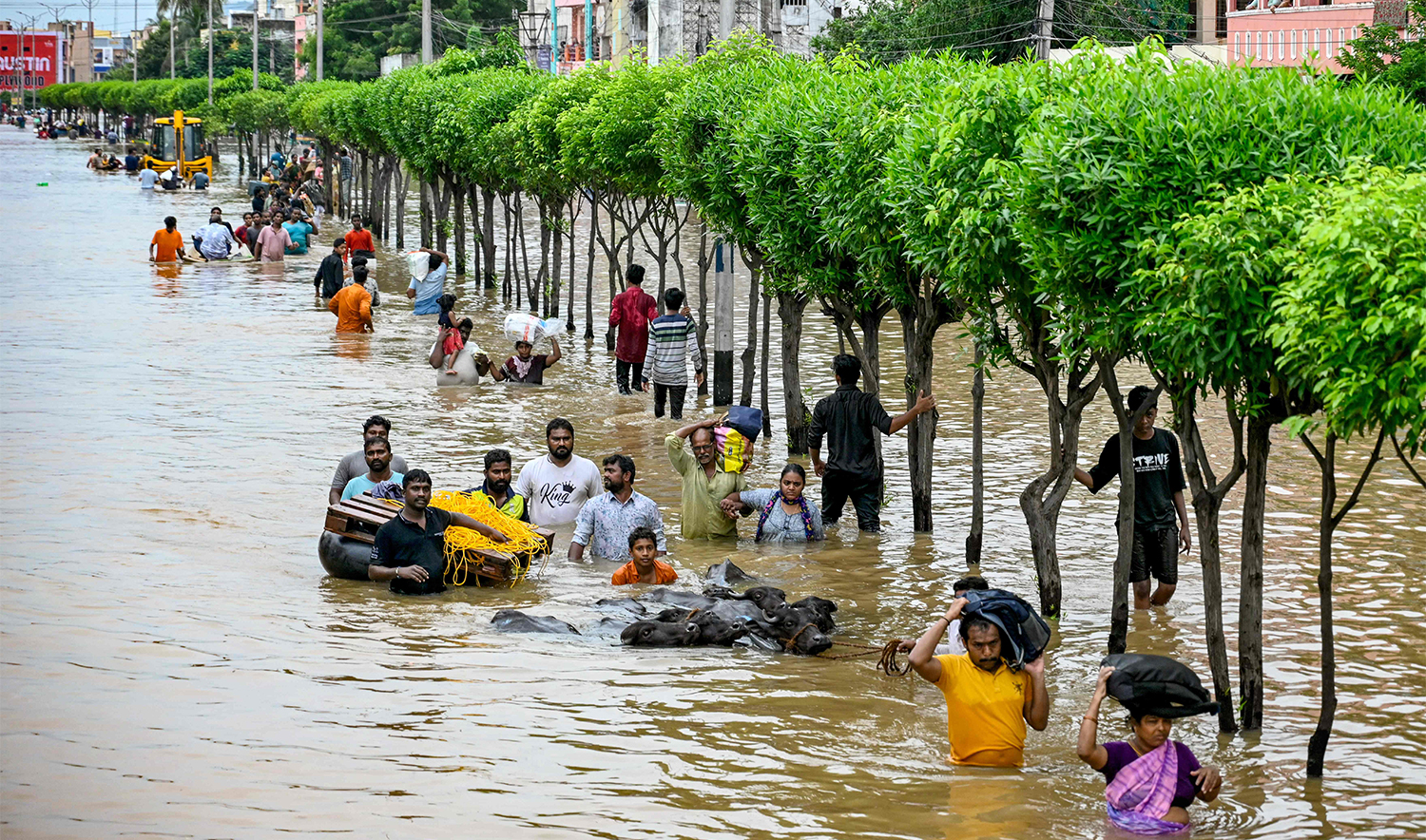 People carry their belongings as they wade through a flooded street after heavy monsoon rains, in Vijayawada on September 2, 2024. (AFP)