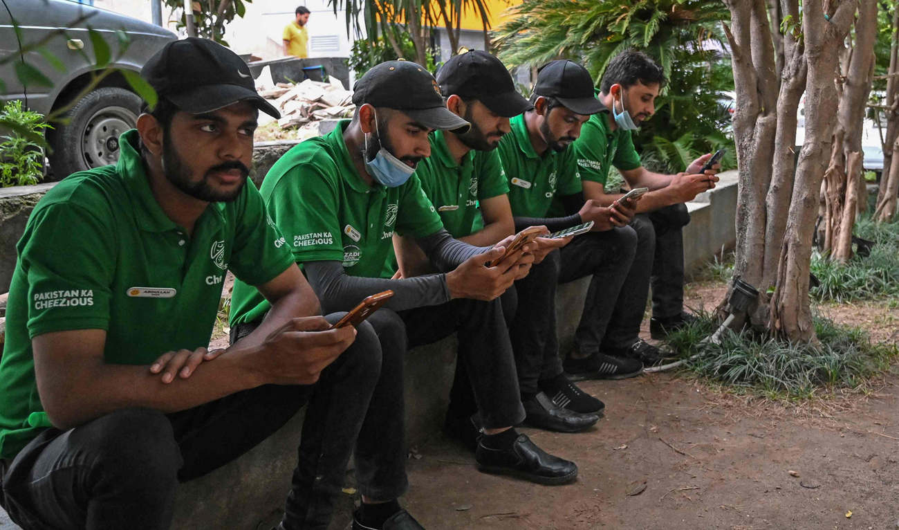 Food delivery men use their mobile phones as they sit near a restaurant in Islamabad on August 17, 2024. (AFP/File)