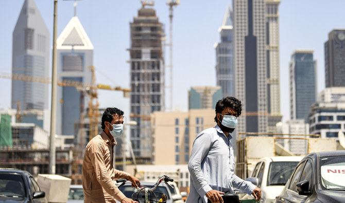 In this file photo, taken on May 6, 2020, foreign workers walk pushing bicycles along a street in the Satwa district of Dubai. (AFP/File)
