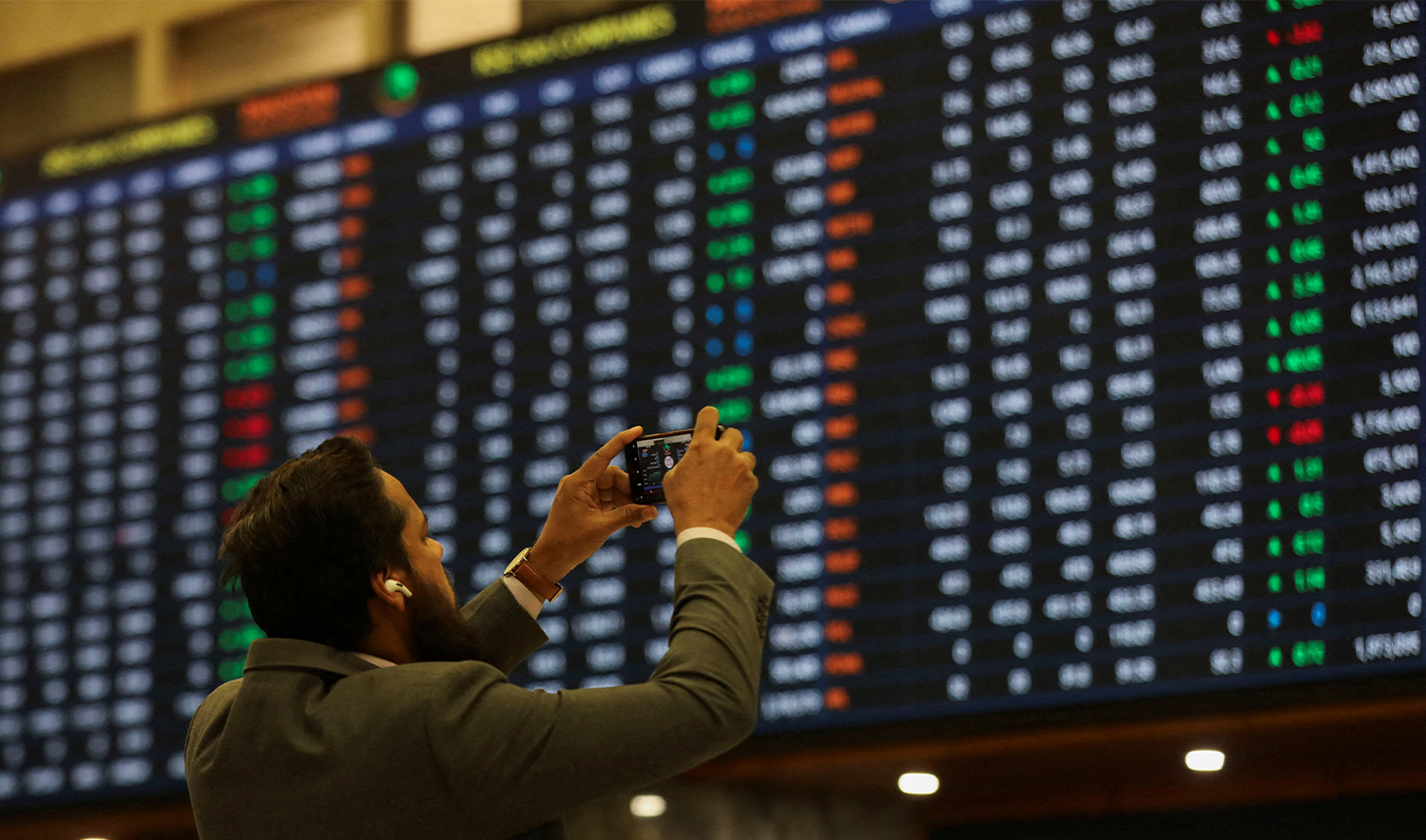 A man uses a mobile phone as he takes a photo of the electronic board displaying share prices during a trading session at the Pakistan Stock Exchange, in Karachi, Pakistan on November 28, 2023. (REUTERS/File)