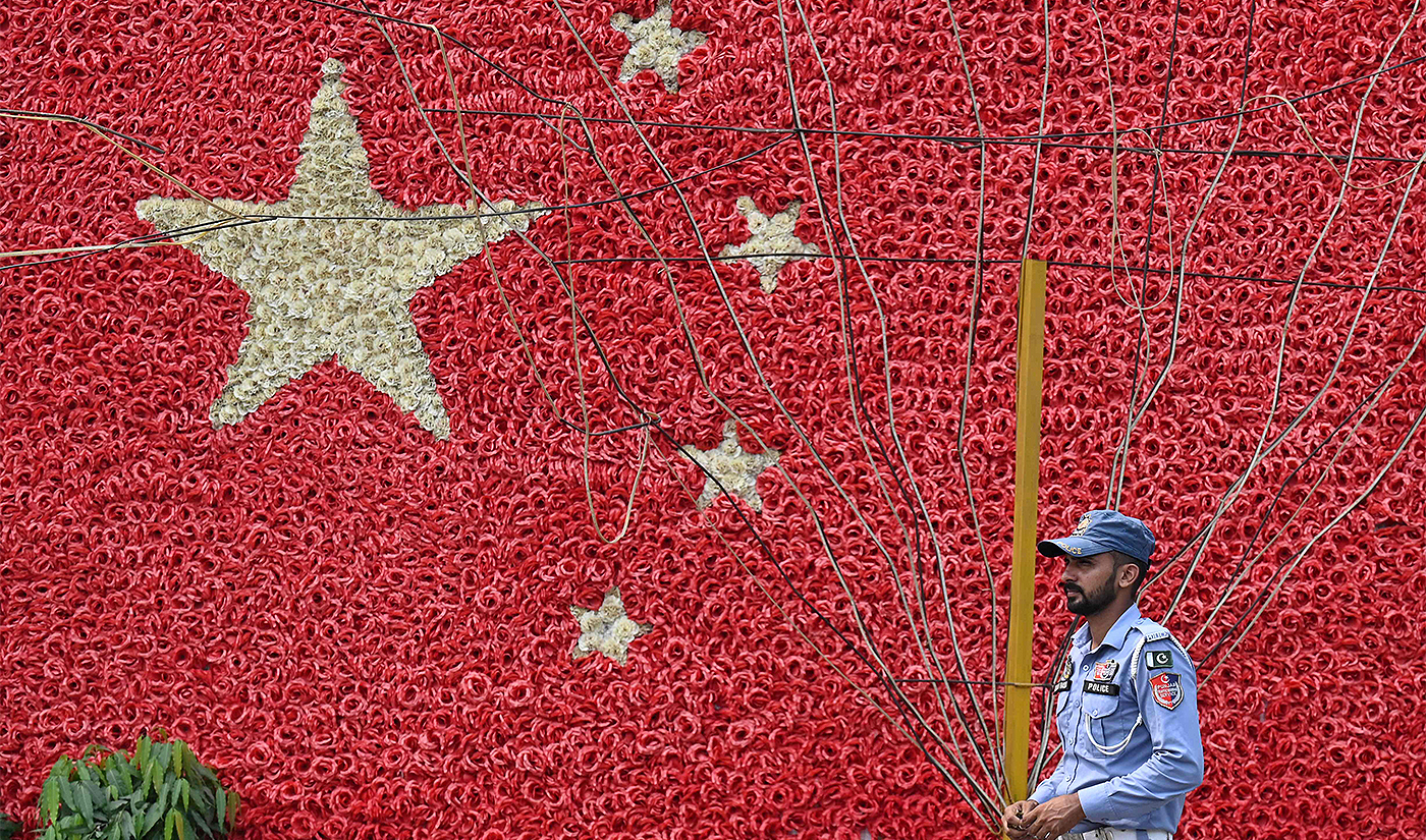 A traffic policeman stands guard next to a wall decorated in the colours of China's national flag along a street in Lahore on September 26, 2024. (AFP)