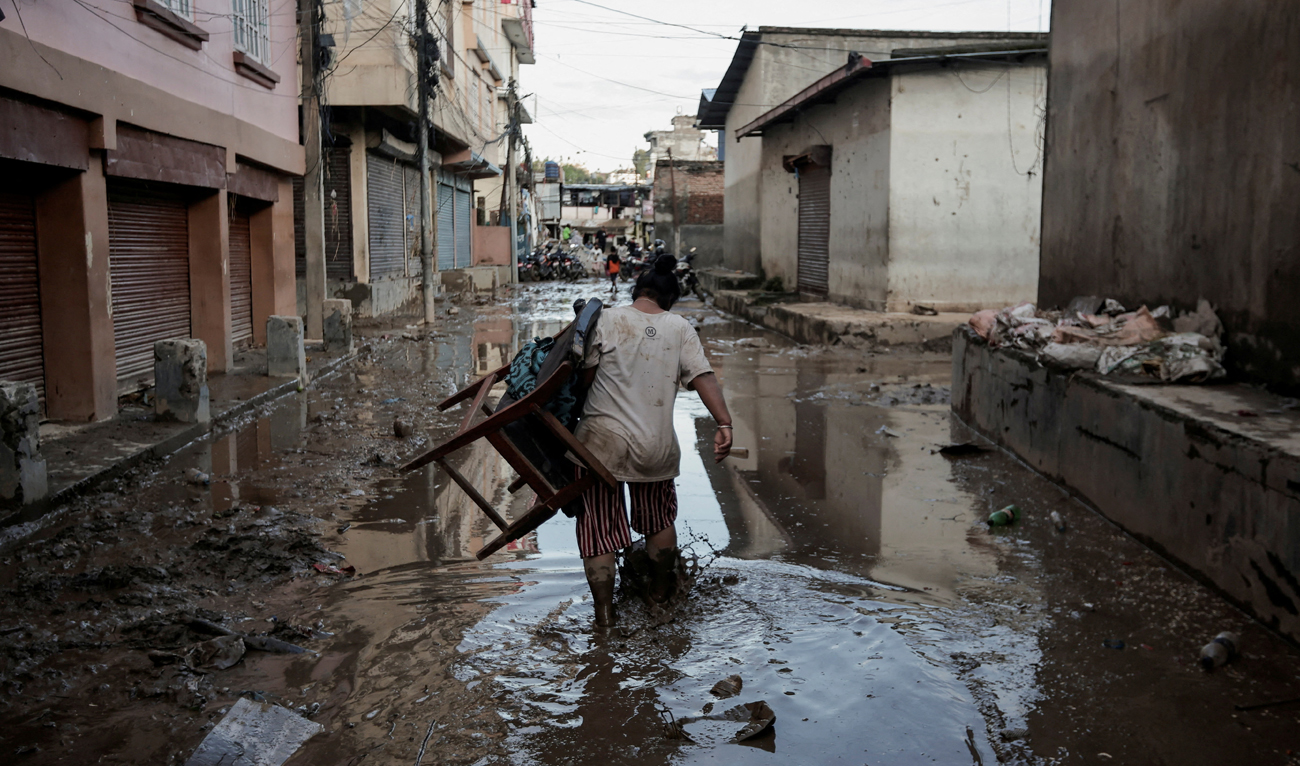 A woman carrying a chair walks along a muddy street as the floodwater recedes from a residential area that was flooded by the overflowing Bagmati River following heavy rains in Katmandu, Nepal on September 29, 2024. (REUTERS)