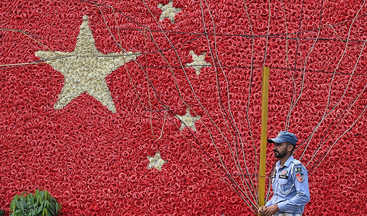 A traffic policeman stands guard next to a wall decorated in the colours of China's national flag along a street in Lahore on September 26, 2024. (AFP)