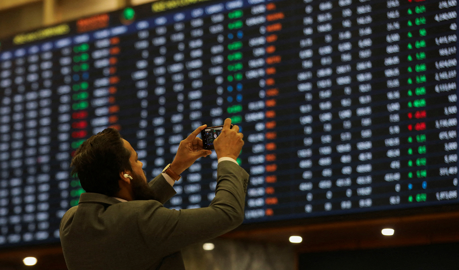 A man uses a mobile phone as he takes a photo of the electronic board displaying share prices during a trading session at the Pakistan Stock Exchange, in Karachi, Pakistan on November 28, 2023. (REUTERS/File)