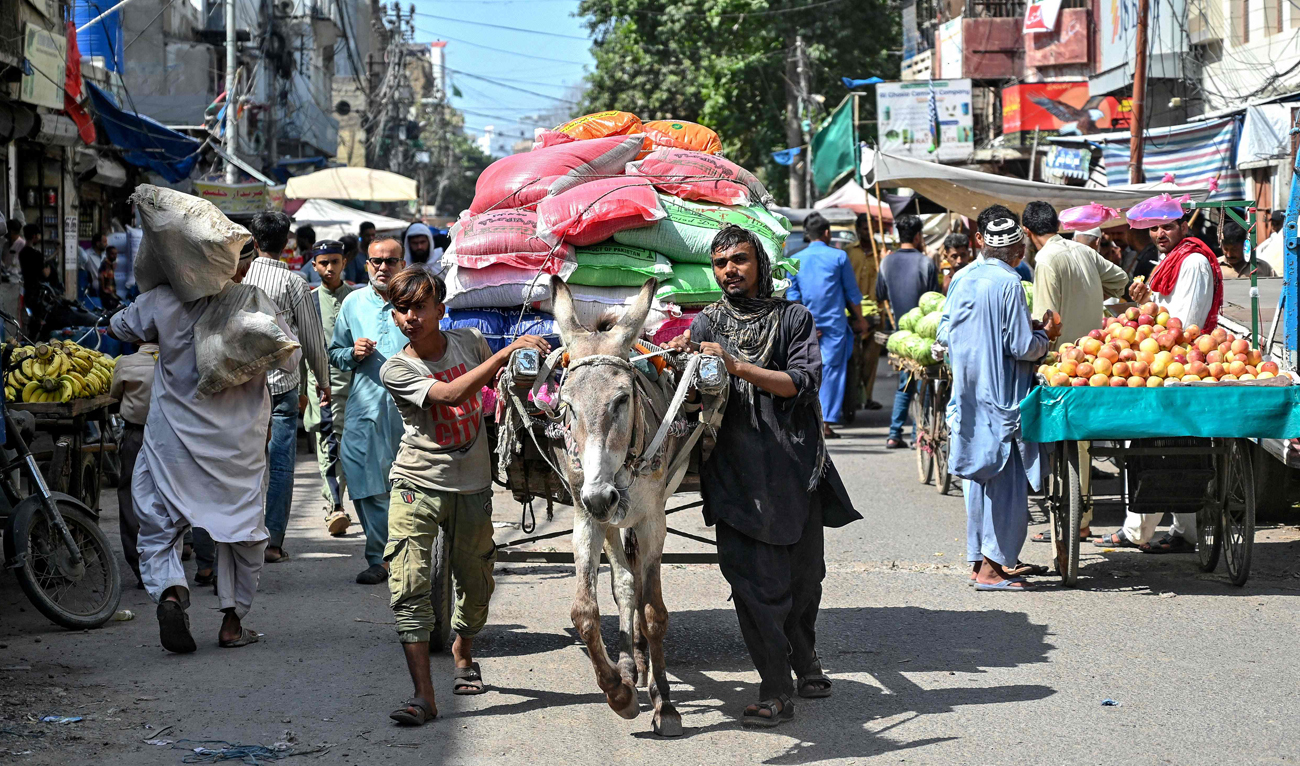 In this photograph taken on October 3, 2024, laborers along with a loaded donkey cart move through a street at a wholesale market in Karachi. (AFP)