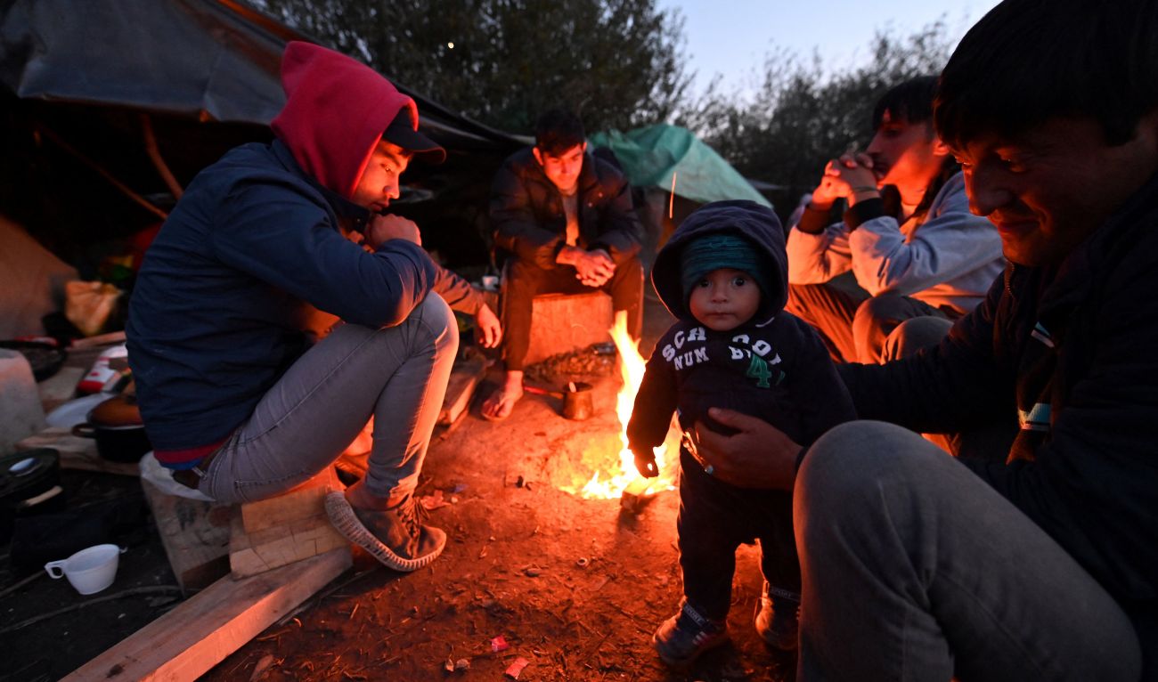 Afghan people are gathered around a fire at an illegal improvised camp, outside Northern-Bosnian border town of Velika Kladusa, on October 15, 2021. (AFP/File)