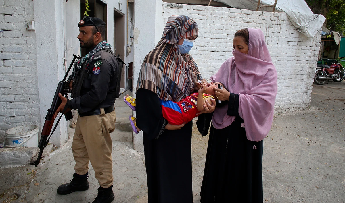 A police officer stands guard as a health worker, right, administers a polio vaccine to a child in a neighborhood of Peshawar, Pakistan, on September 9, 2024. (AP/File)