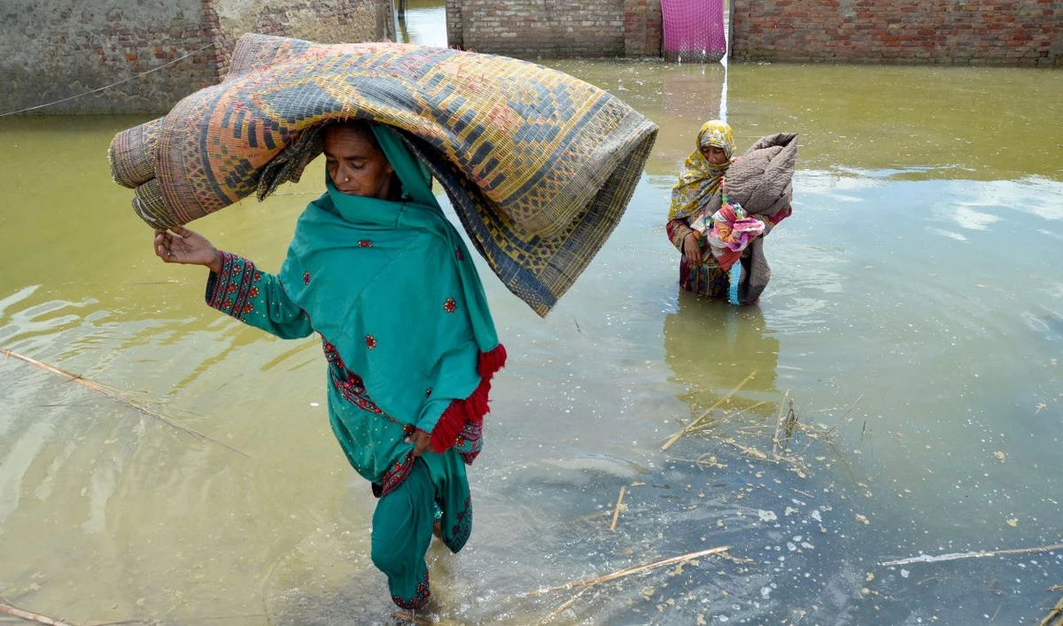 Women displaced by flood, carry their belongings as they wade through floodwaters after heavy monsoon rains at Sohbatpur in Jaffarabad district, Balochistan province on August 19, 2024. (AFP/File)