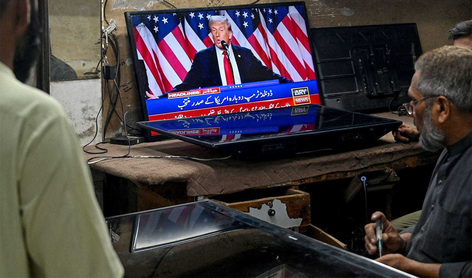 Men watch a television broadcast featuring US former president and Republican presidential candidate Donald Trump at a workshop in Karachi on November 6, 2024. (AFP)