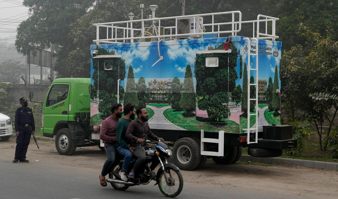 A motorcyclist rides past a mobile automatic air quality monitoring station parking along a roadside to mentor air quality index, in Lahore on November 14, 2024. (AP)