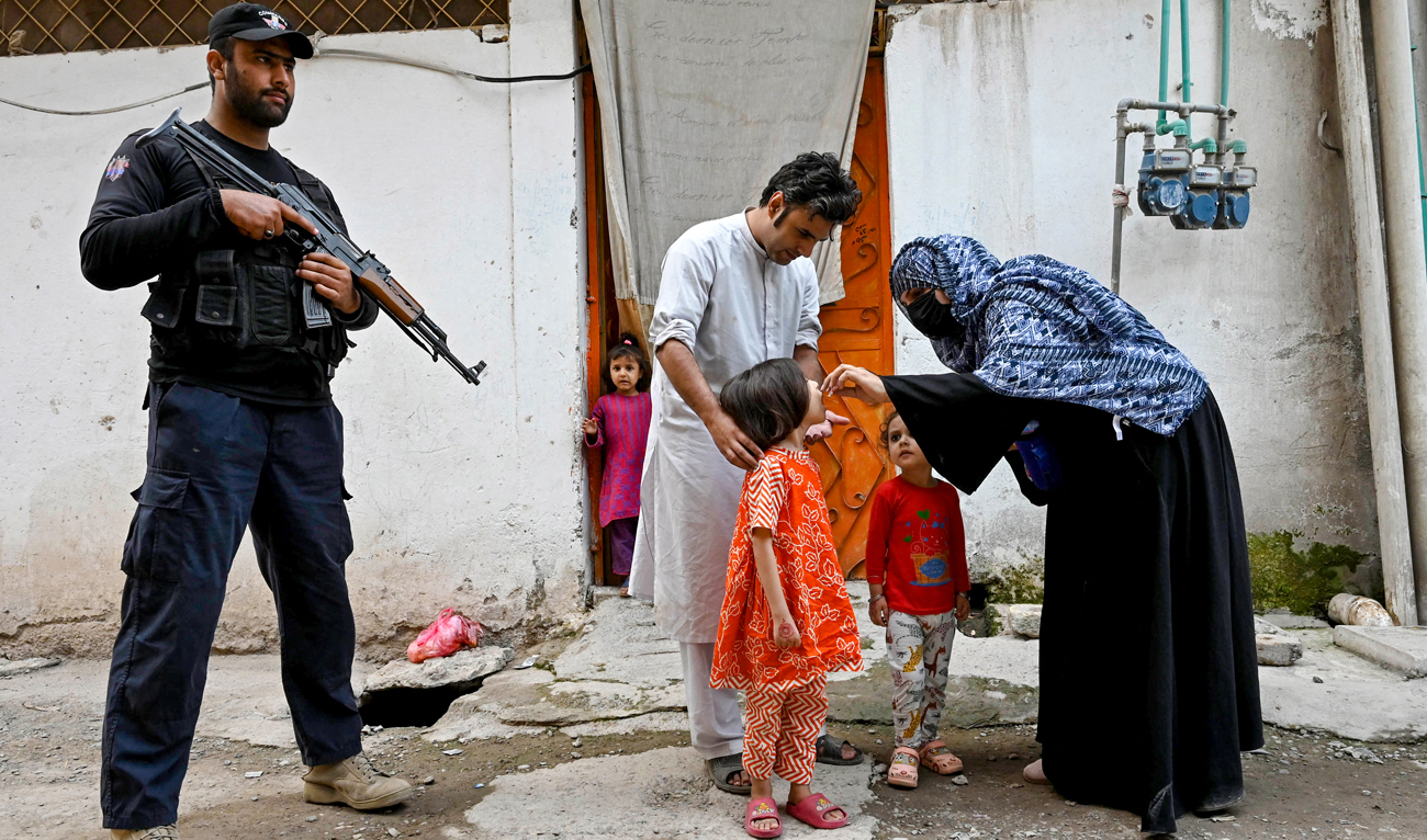 This photograph taken on October 29, 2024 shows an elite police personnel (L) standing guard as a health worker (R) administers polio drops to a child during a door-to-door poliovirus vaccination campaign on the outskirts of Peshawar. (AFP)