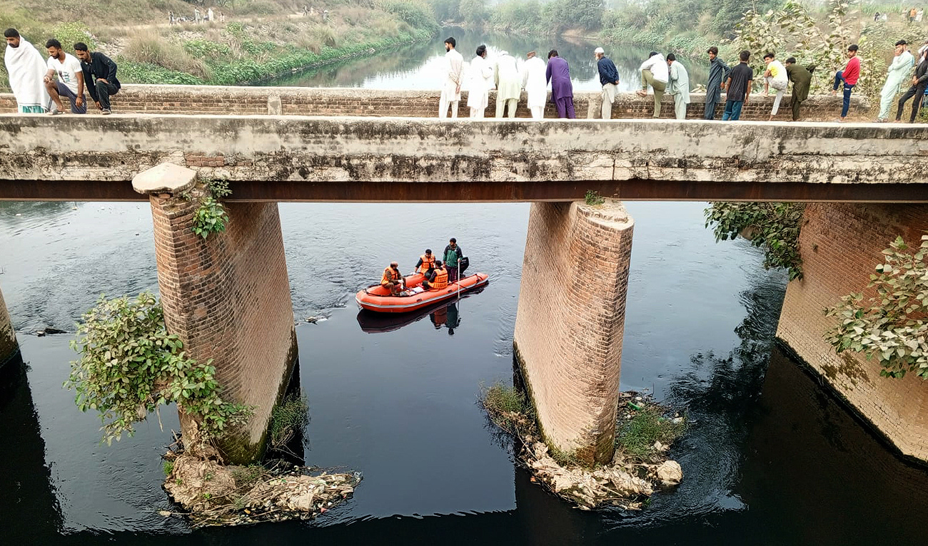 In this handout photo, taken and released by Rescue 1122 emergency service on November 18, 2024, bystanders look as Pakistani rescuers recover body of a 30-year-old woman from drain in Daska. Four family members accused of murdering the woman in Punjab province have been arrested, according to police. (Photo courtesy: Rescue1122)