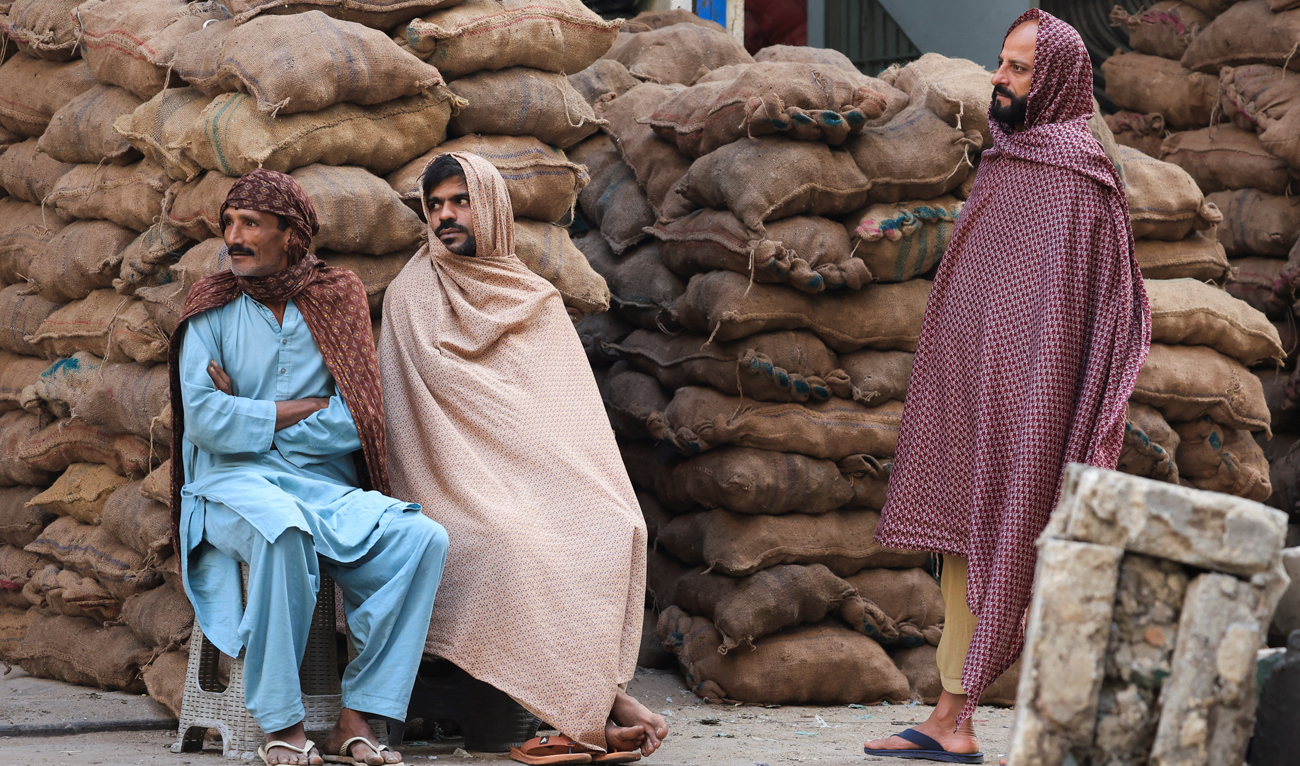 Laborers cover themselves with shawls to protect themselves from the cold during the early morning, as they wait for work at the market in Karachi on December 26, 2024. (REUTERS/File)