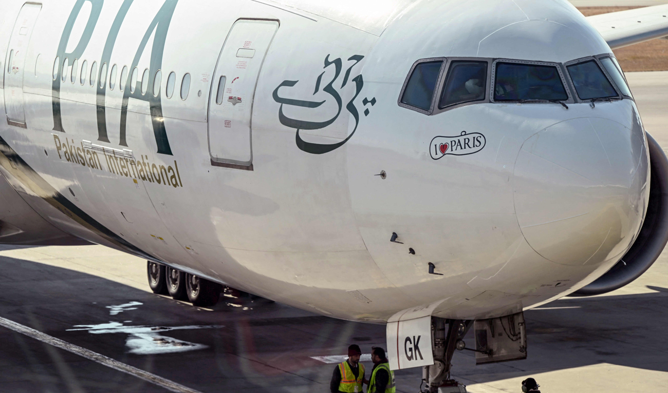 Ground staff stand next to the Pakistan International Airline (PIA) aircraft ahead of its takeoff for Paris at the Islamabad International Airport on January 10, 2025, as EU authorities lift a four-year ban on the state airline. (AFP/File)