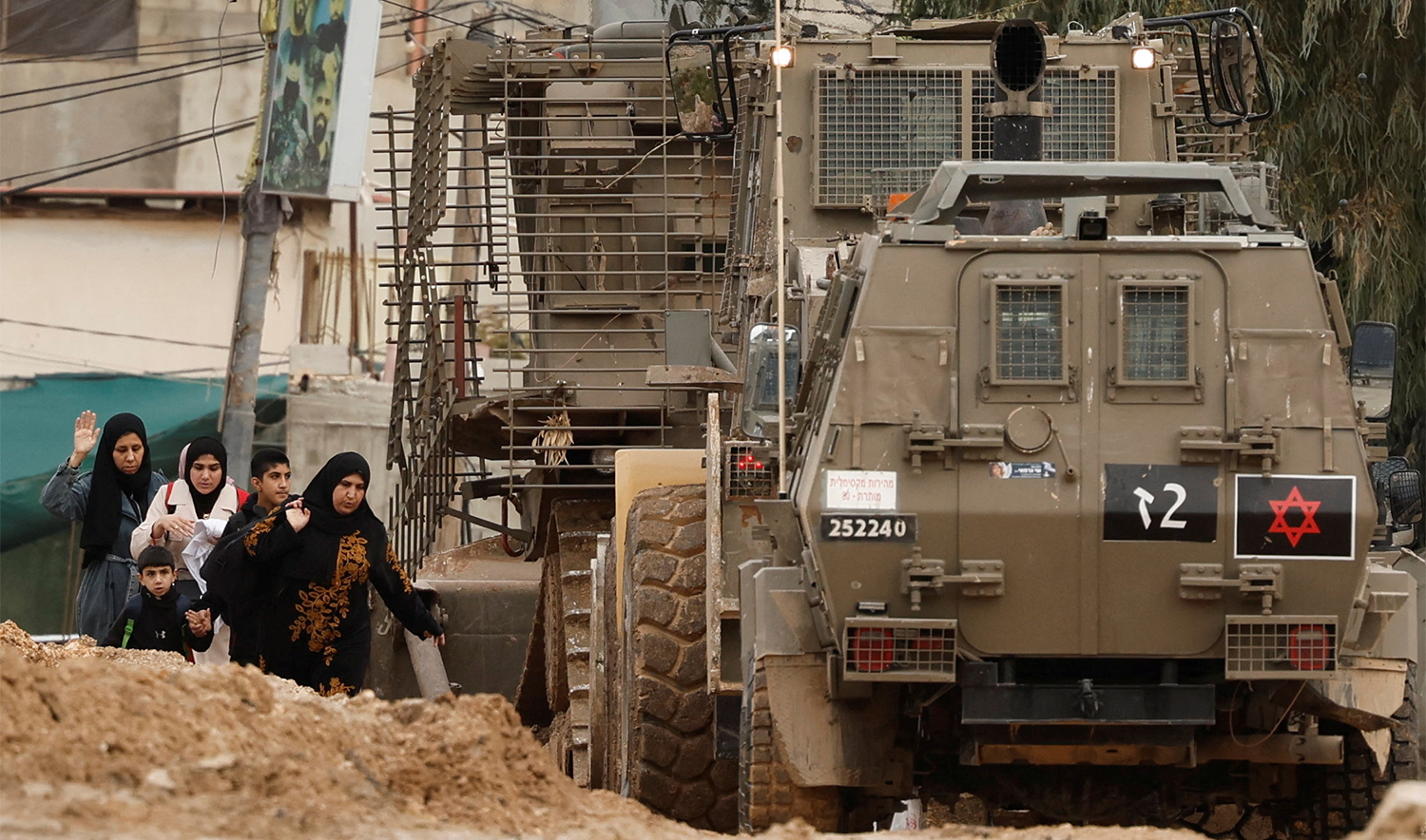 Palestinians walk next to heavy machinery and armored vehicles on a damaged street as they leave Jenin camp during an Israeli raid, in the Israeli-occupied West Bank, on January 22, 2025. (REUTERS)