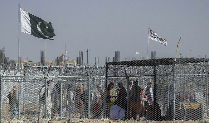 Afghan and Pakistani nationals walk through a security barrier to cross the border as a national flag of Pakistan and a Taliban flag is masted in the Pakistan-Afghanistan border crossing point in Chaman on August 24, 2021. (AFP/File)