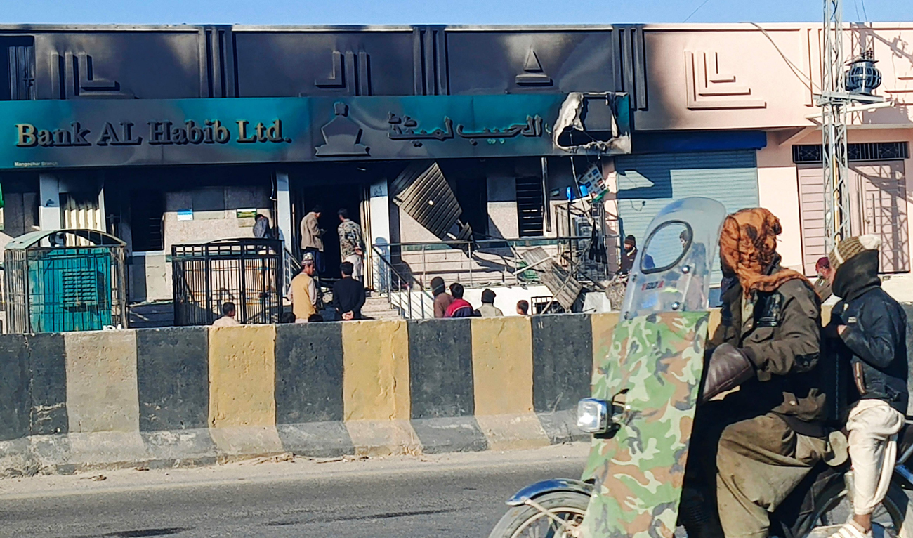 Commuters ride past a bank set ablaze by militants at Kalat district, in Pakistan's Balochistan province on February 1, 2025. (AFP)