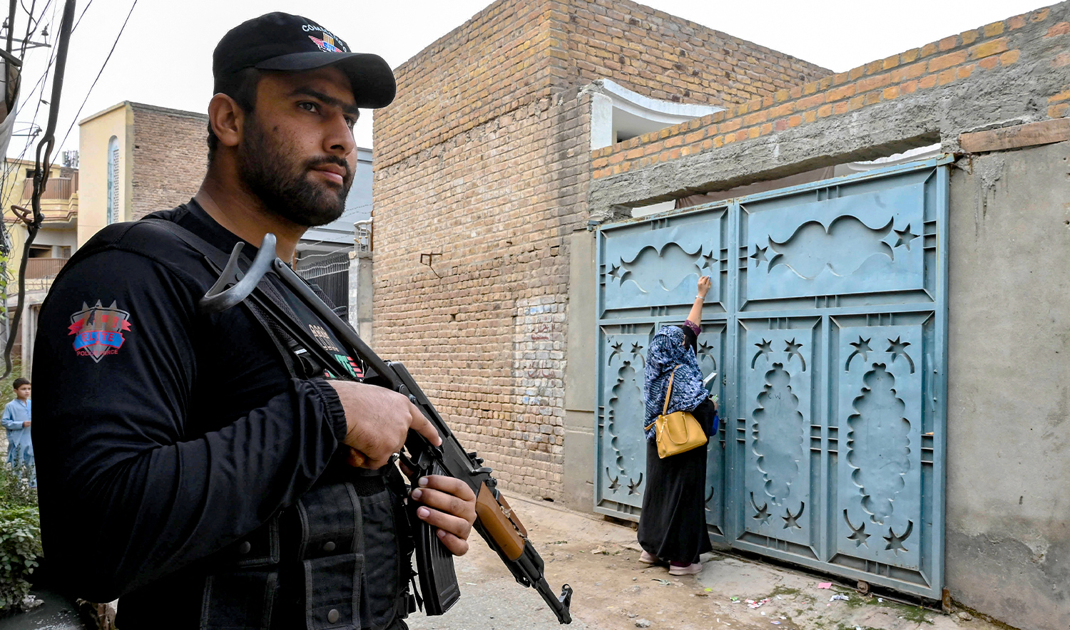 This photograph taken on October 29, 2024 shows an elite police personnel (L) standing guard as a health worker marks houses with numbers during a door-to-door poliovirus vaccination campaign for children on the outskirts of Peshawar. (AFP/File)